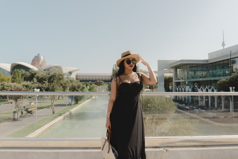 Stylish woman in a black dress and hat enjoying a sunny day in Baku, Azerbaijan.