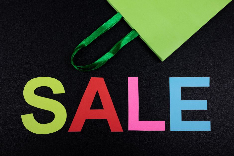 Close-up of colorful SALE letters on black background with green shopping bag.