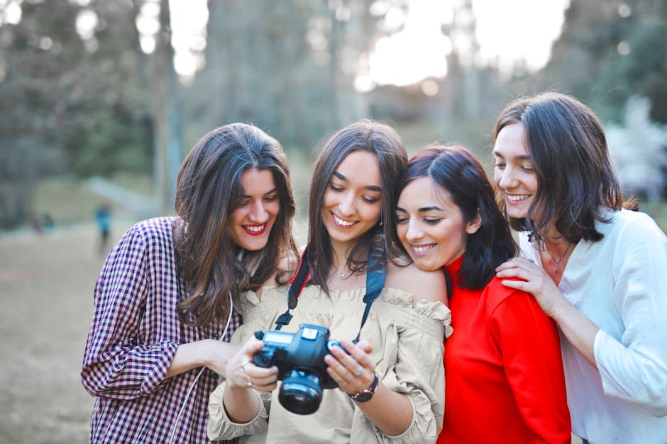 Four happy women sharing a moment outdoors, looking at photos on a DSLR camera.