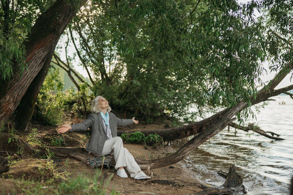 Senior woman peacefully meditating by a tranquil lakeshore with arms open.