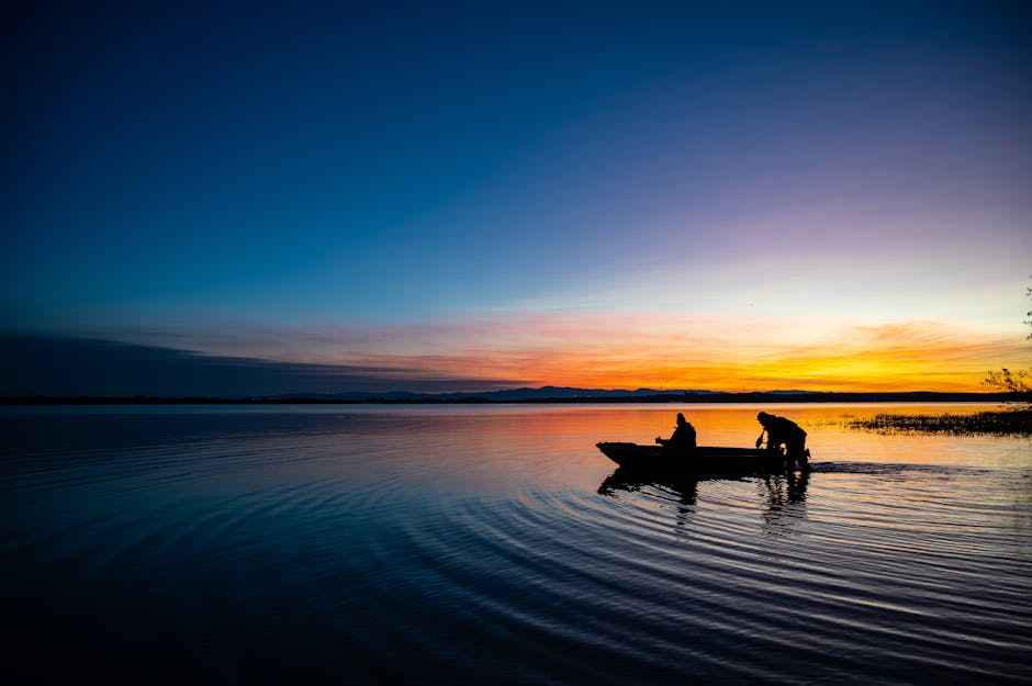 Silhouette of fishermen on a boat during a vibrant sunset over a peaceful lake.