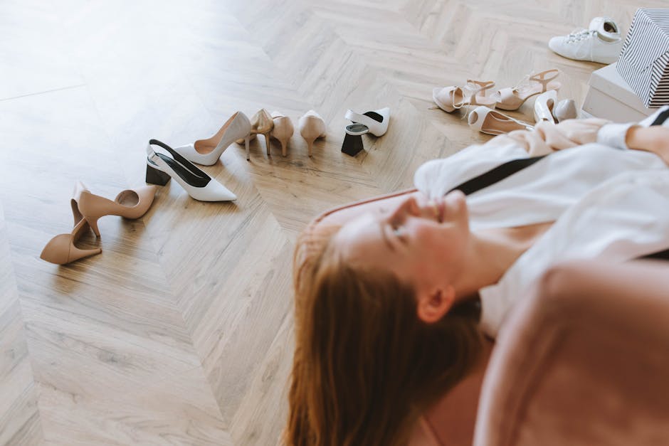 Woman relaxing on a couch with various high heel shoes around her on a wooden floor.