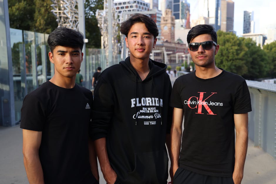 Three young adults posing casually outdoors with an urban skyline in the background.