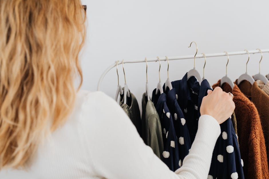 A woman browses clothing in a boutique, focusing on a rack of hanging garments.