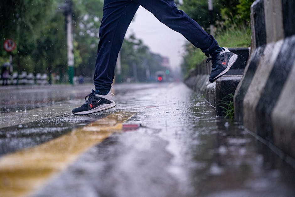 Dynamic image of a person jumping over a puddle during a light rain, showcasing athletic footwear.