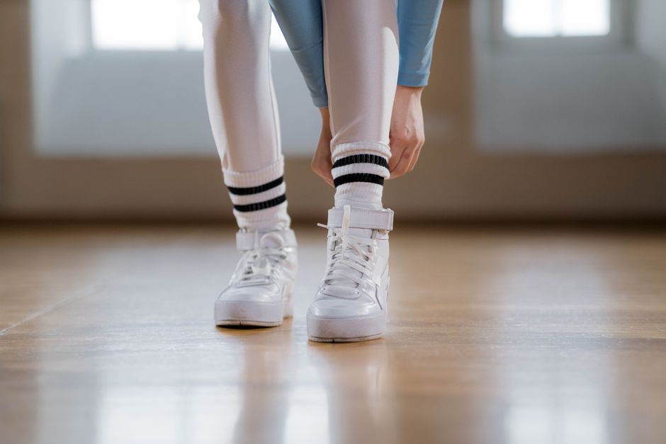 Close-up of a person tying white sneakers indoors, wearing leggings and striped socks.
