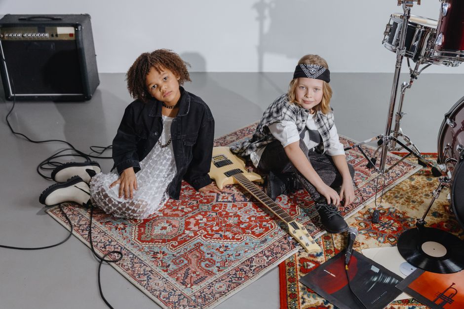 Two children sitting on a rug in a studio with musical instruments, embracing a rockstar vibe.