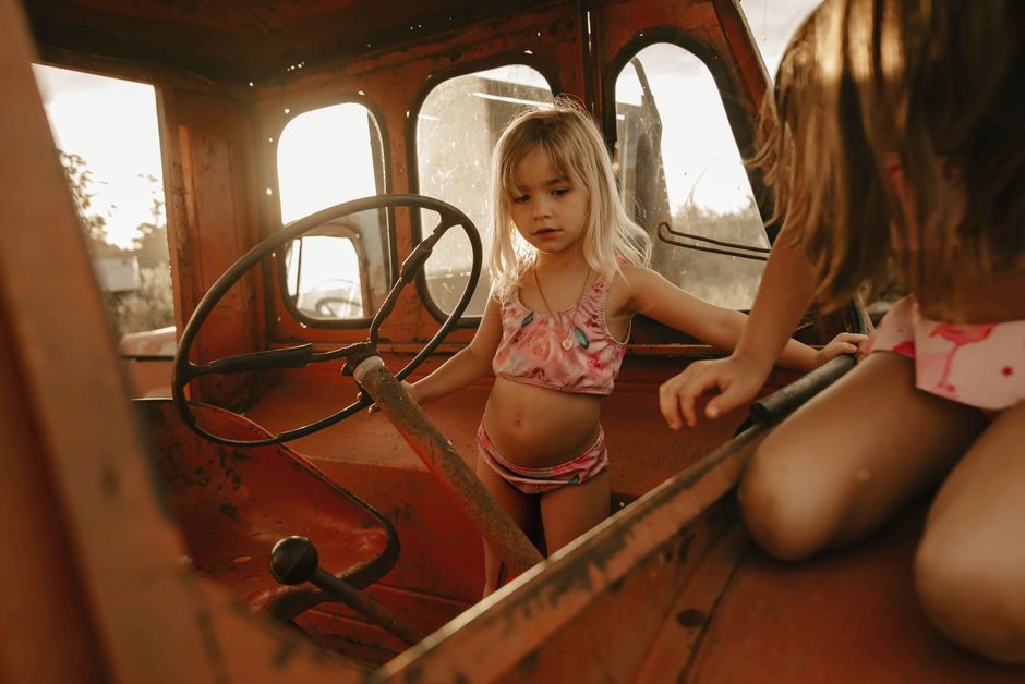 Two young girls explore inside a vintage tractor cabin, bathed in warm sunlight.
