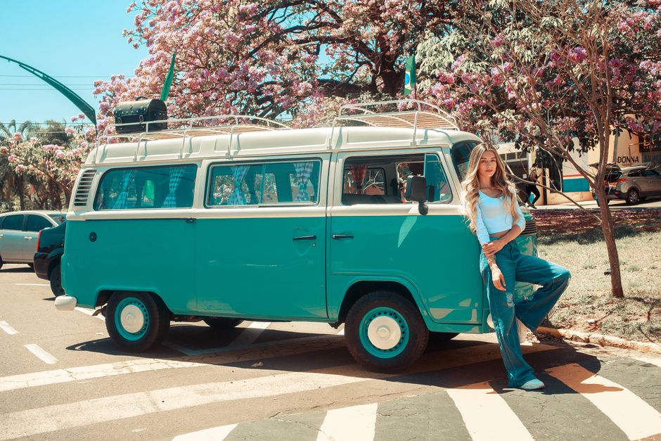 Woman in casual attire leaning on a vintage teal van on a sunny spring day.
