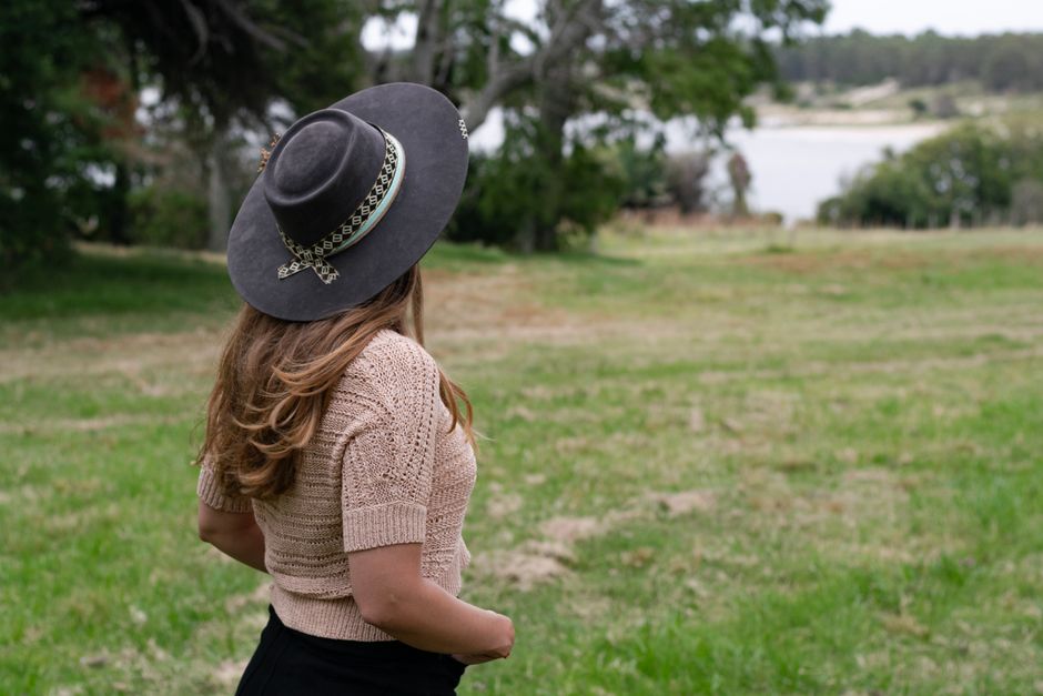 A woman wearing a stylish hat enjoys a peaceful view of a rural Uruguay landscape.