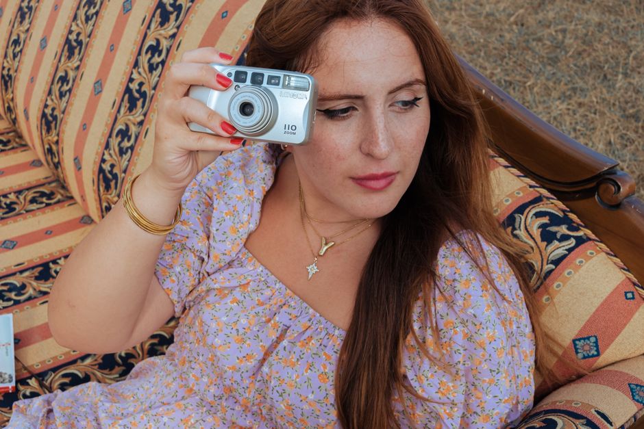 Woman holding a vintage camera on a patterned couch outdoors. Bohemian style.
