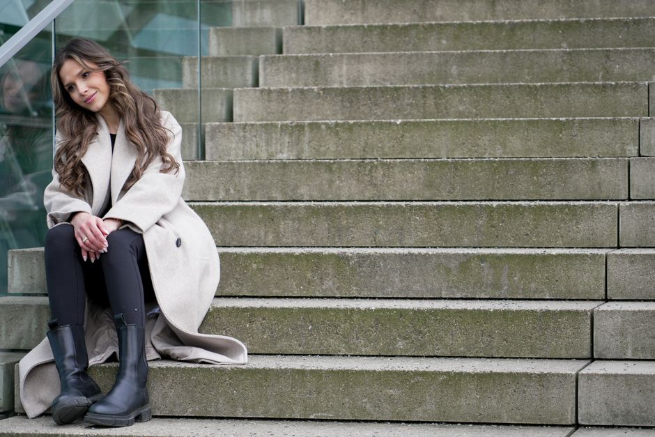 Woman in fashionable coat and boots sitting on stairs in Berlin, capturing a modern urban vibe.