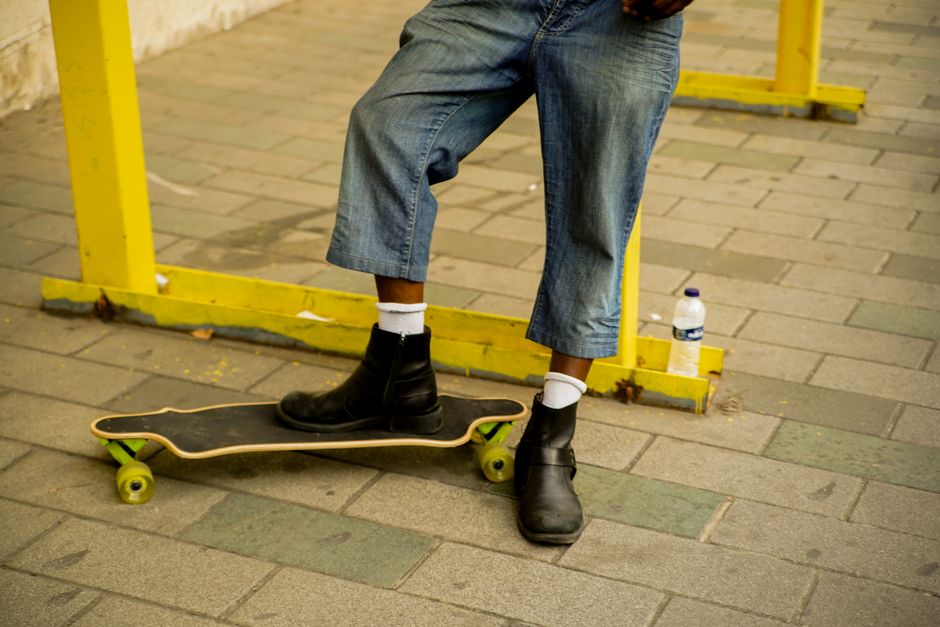Portrait of a skater's legs wearing boots and jeans with a skateboard on an urban sidewalk.