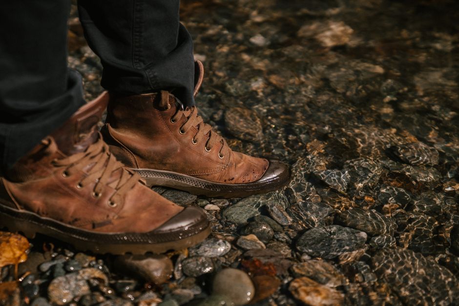 Crop unrecognizable person in autumn boots and black jeans standing near water in forest