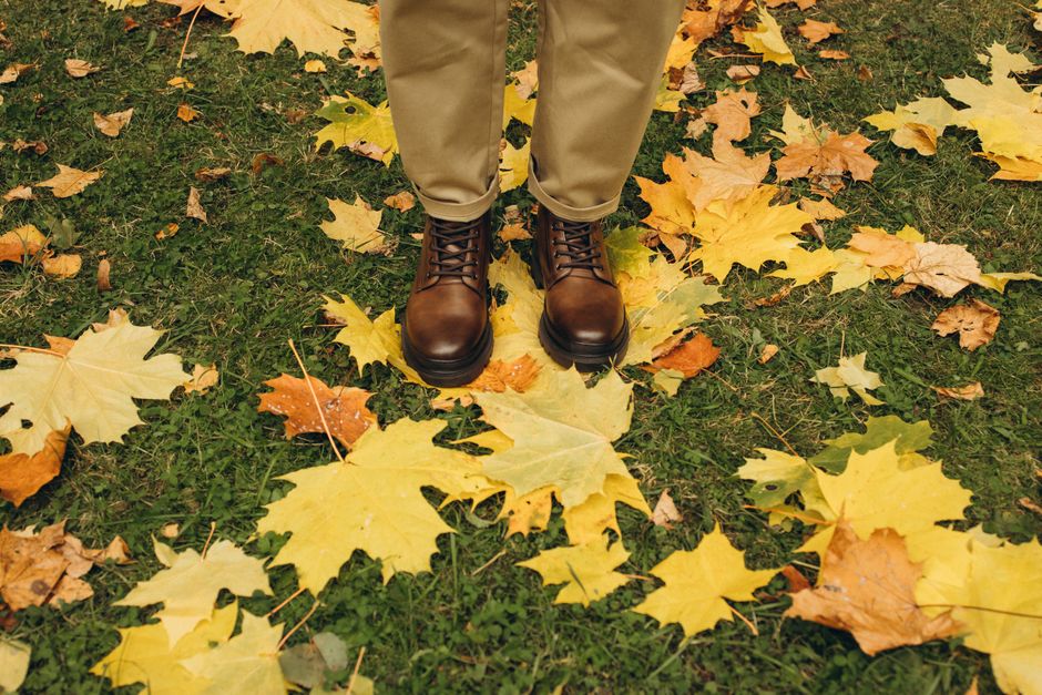 Close-up of brown leather shoes on fallen autumn leaves in a park setting.
