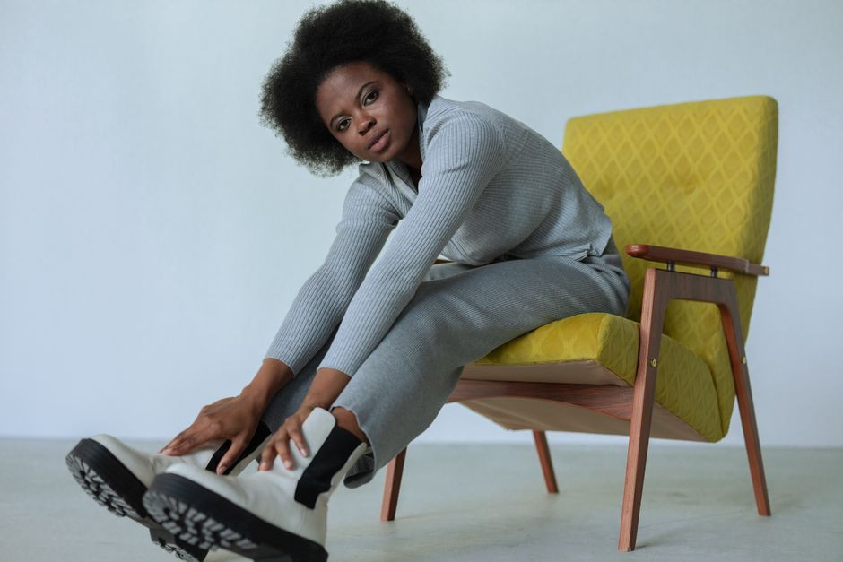 Fashionable woman with afro hair posing indoors in a modern chair.