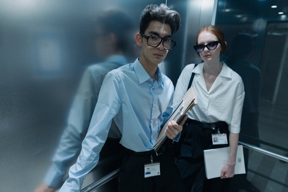 Two serious professionals standing inside an elevator, striking poses.