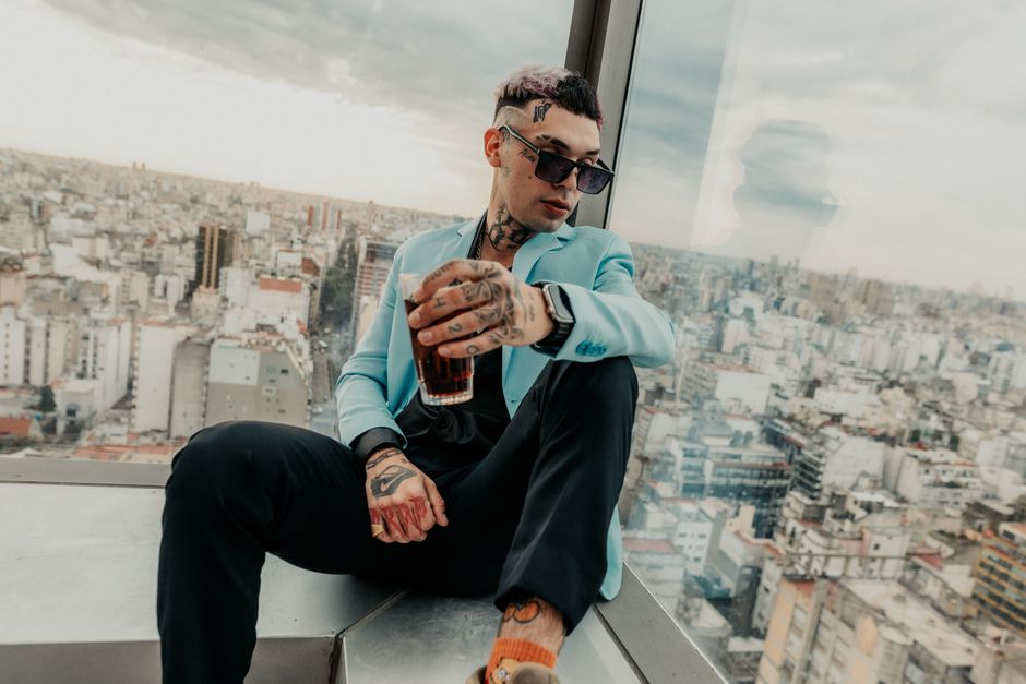 Man in blue suit and sunglasses enjoys drink with cityscape view in Buenos Aires.