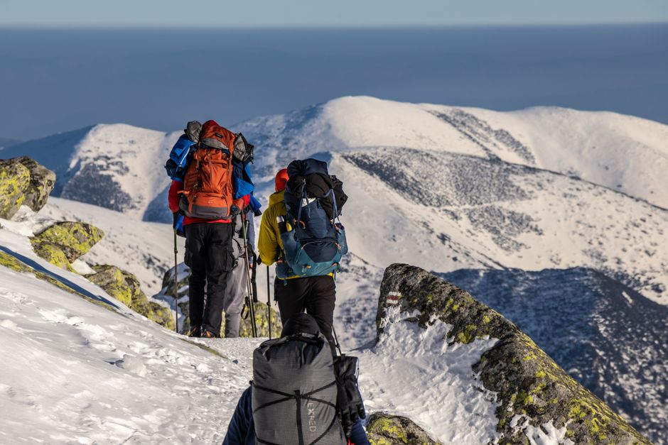 Adventurous hikers trek through a snowy mountain landscape with backpacks. Clear skies and rugged scenery.