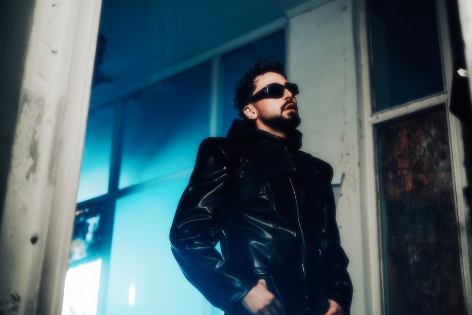 Portrait of a man in a leather jacket and sunglasses, exuding confidence indoors.