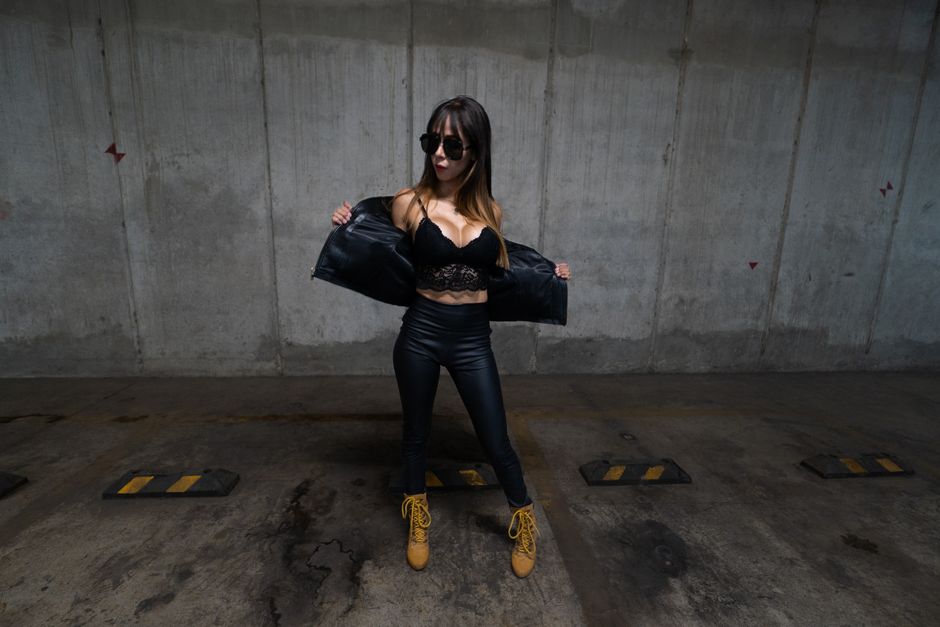 Trendy woman in leather outfit and sunglasses posing confidently in an underground parking lot.