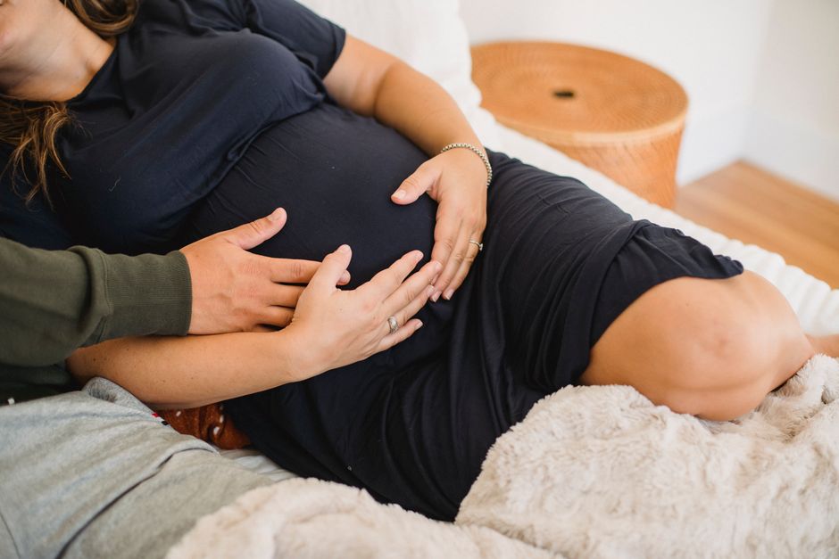 From above of crop anonymous man caressing tummy of pregnant wife while resting on soft bed at home