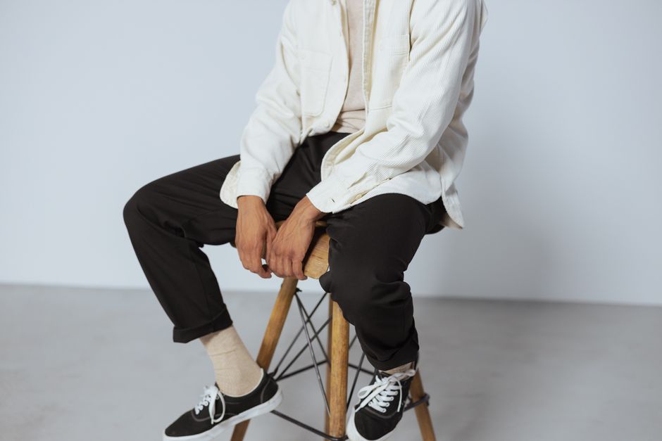 A person dressed in casual modern fashion sits on a wooden stool indoors.