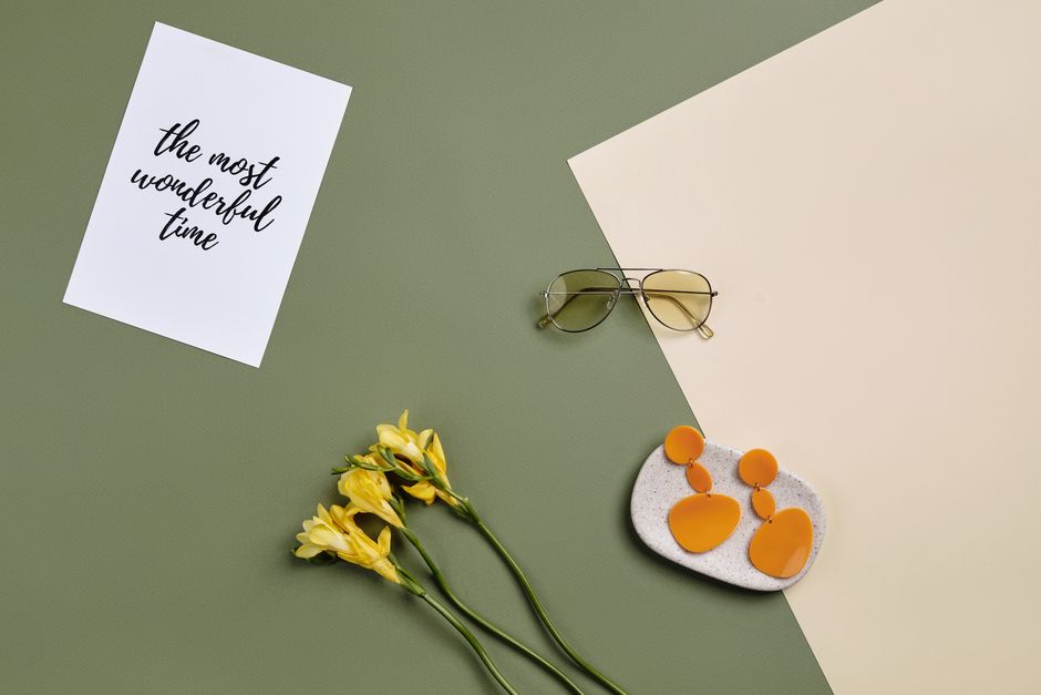 A chic summer flat lay featuring sunglasses, earrings, and flowers on colored paper.