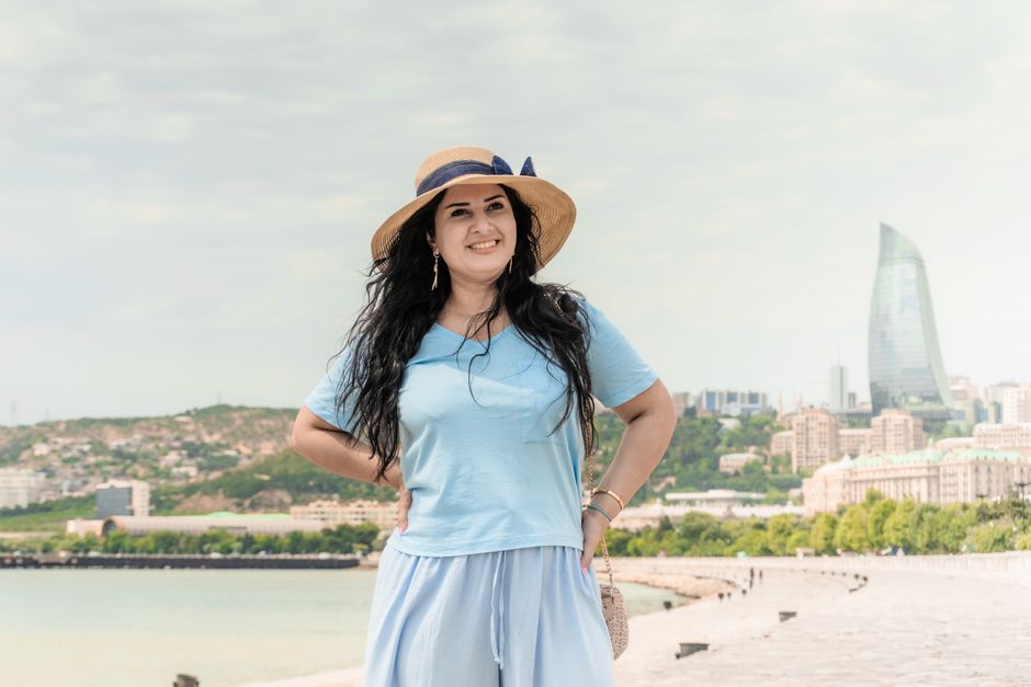 A woman wearing a light blue dress and straw hat smiling with the iconic Flame Towers in Baku, Azerbaijan.
