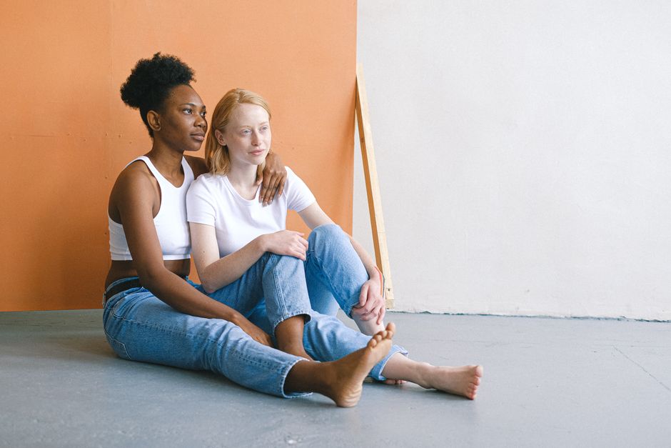 Interracial lesbian couple sitting on the floor in casual attire, radiating love and togetherness.