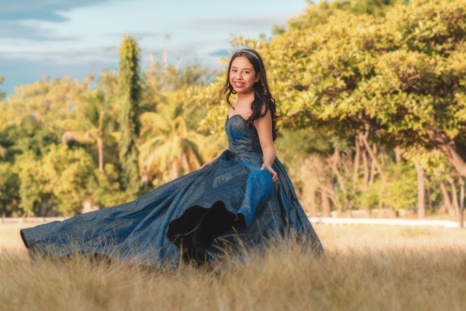 Elegant portrait of a young woman in a blue dress posing gracefully in a sunny meadow.