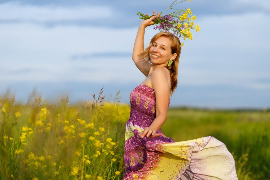 A smiling woman in a vibrant dress holding flowers in a sunny meadow