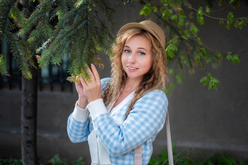 Charming blonde woman in casual attire posing with evergreen branches outdoors.
