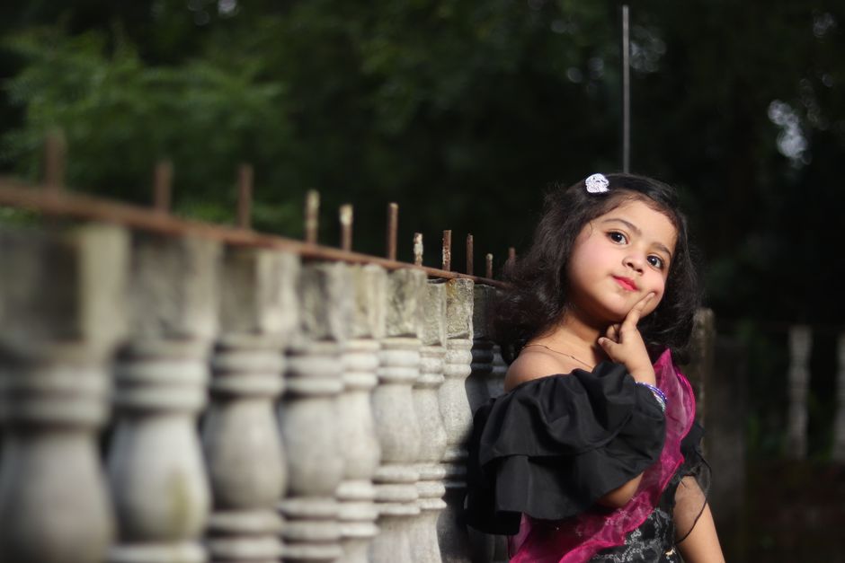 Charming young girl posing outdoors against a stone railing in Bangladesh.
