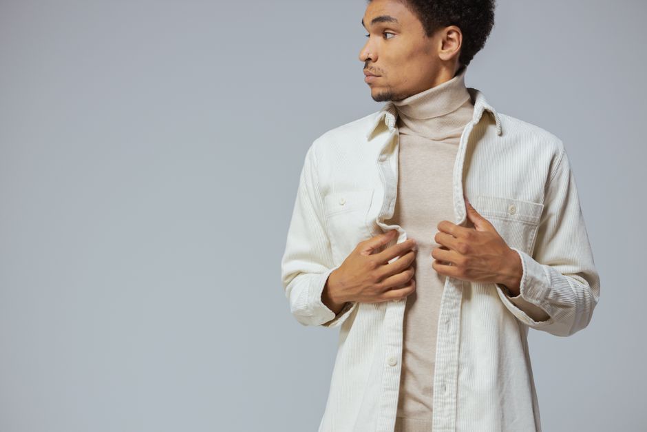 Man posing in neutral turtleneck and dress shirt with hands on collar, looking sideways.