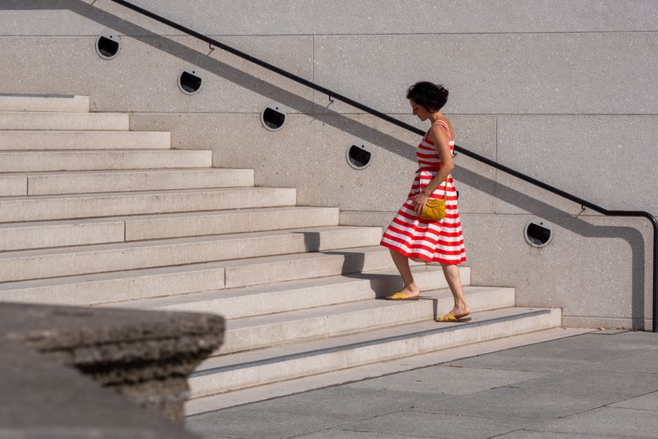 A woman in a red and white striped dress ascends a stone staircase outdoors.
