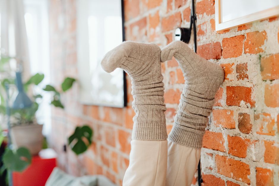 Comfortable feet with grey knit socks resting against a brick wall indoors.
