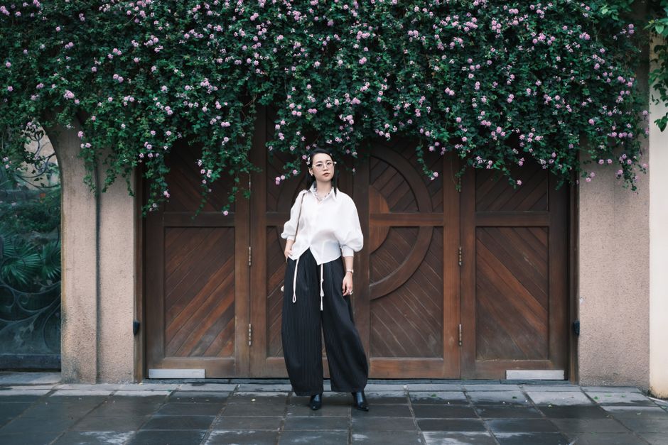 A fashionable woman poses in front of a wooden door adorned with climbing flowers.