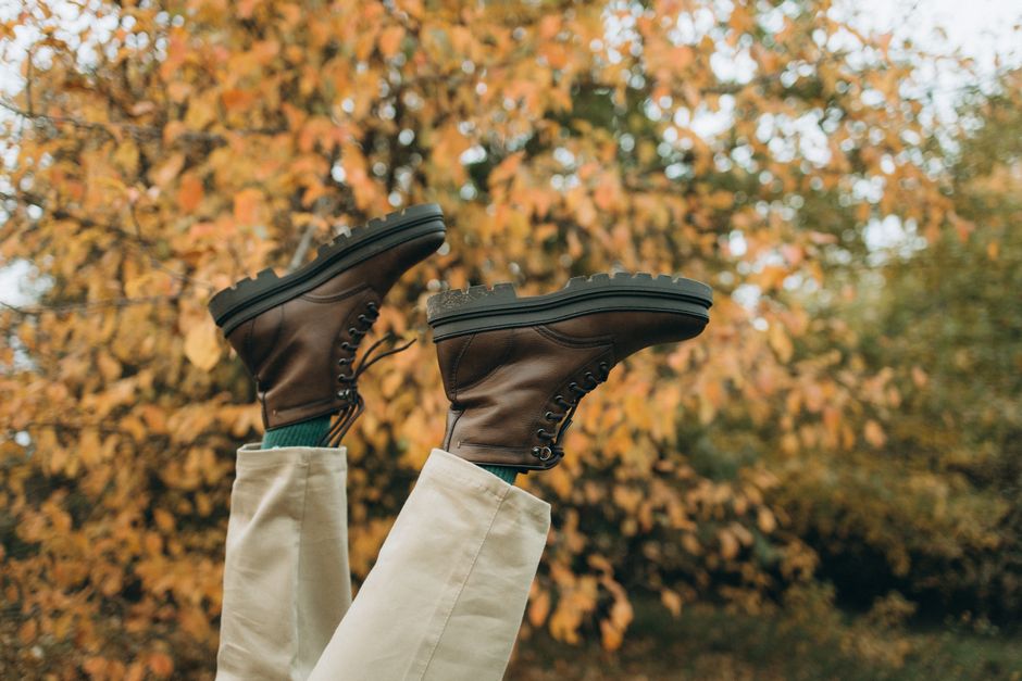 Close-up of legs with leather boots against vibrant autumn foliage background.